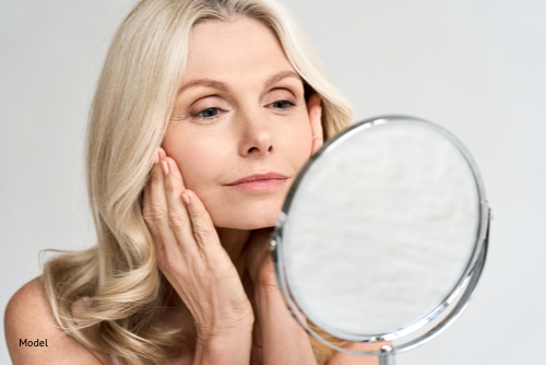 Mature blonde woman looking at her face in a small mirror
