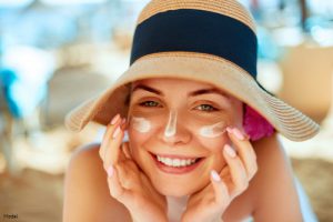 Smiling woman outdoors in a beach hat with sunscreen on her cheeks and nose