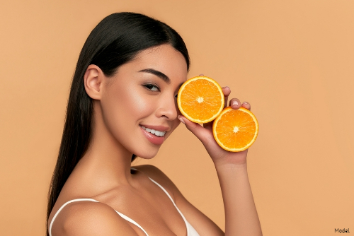 Woman with clear skin holding two halves of an orange