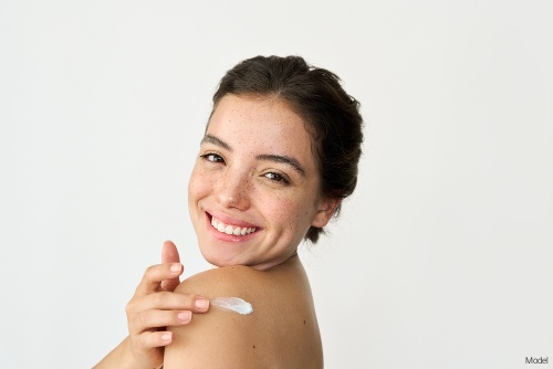 Joyful woman smiling and applying sunscreen to her shoulder