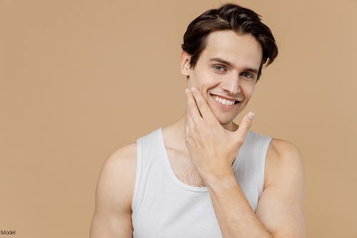 Confident, clean-shaven man smiling while rubbing his chin