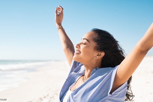 Confident woman with arms stretched up into the air at the beach smiling with eyes closed